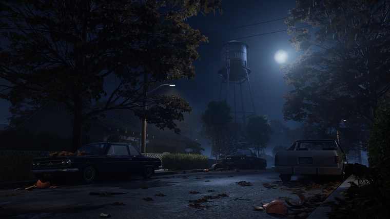 A dark residential street with a water tower rising behind the trees